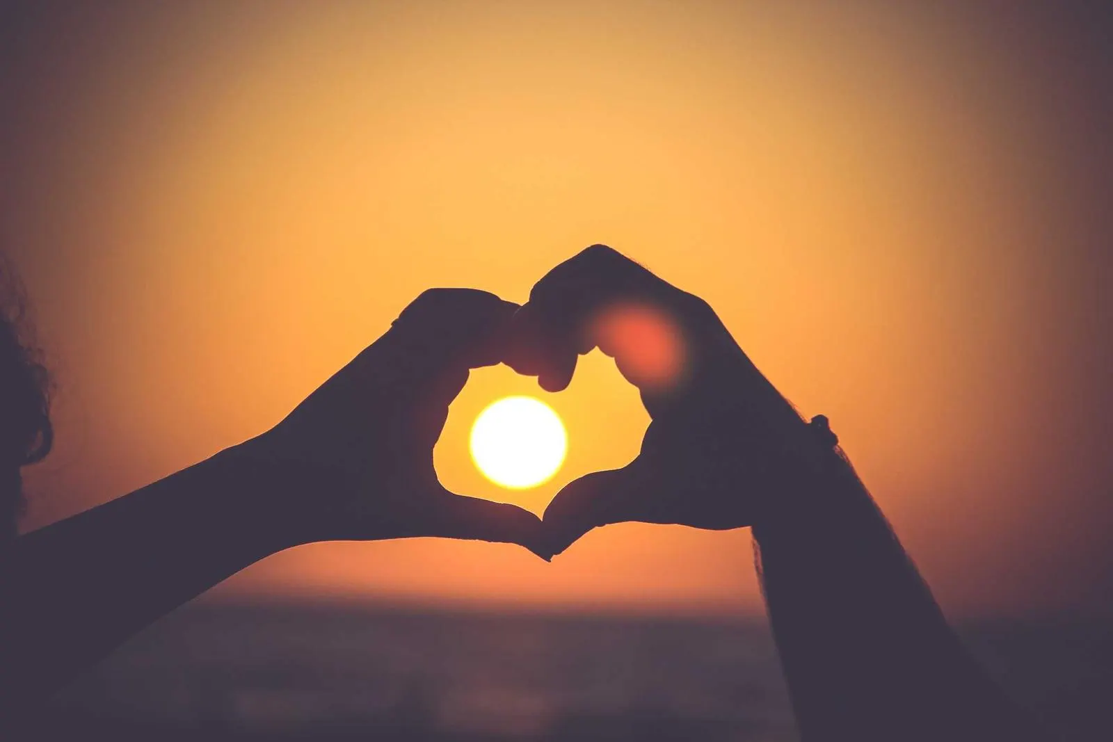 Two hands making a heart shape against the sunset