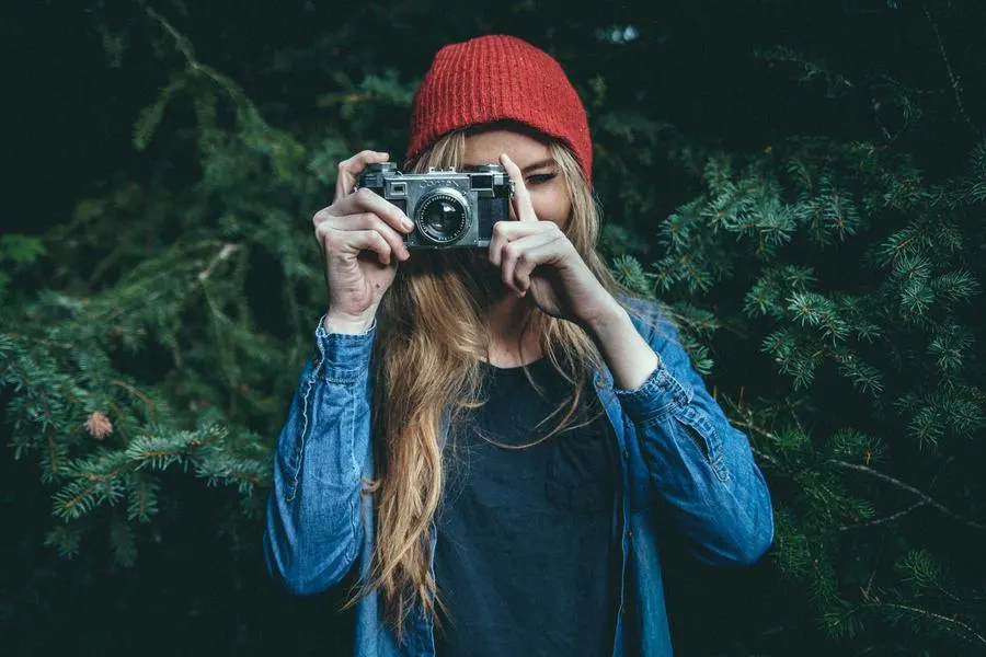 Mara Lindqvist with her camera, in a red hat, in a pine forest